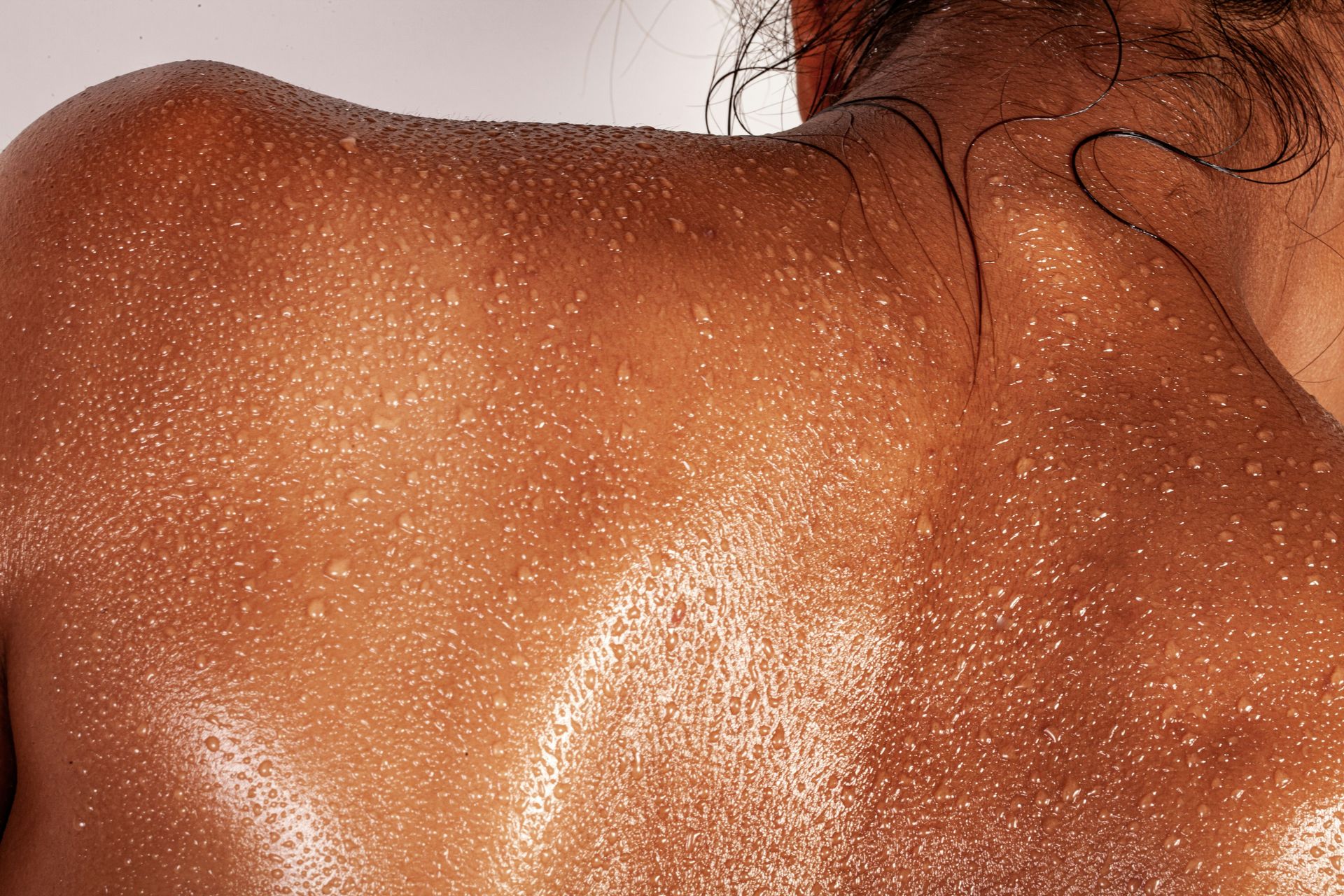 A person's back covered in beads of sweat with dark hair at the neck